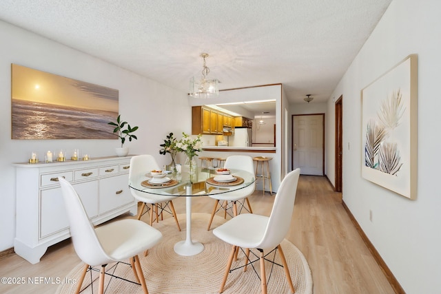 dining area featuring a textured ceiling, light hardwood / wood-style floors, and a notable chandelier