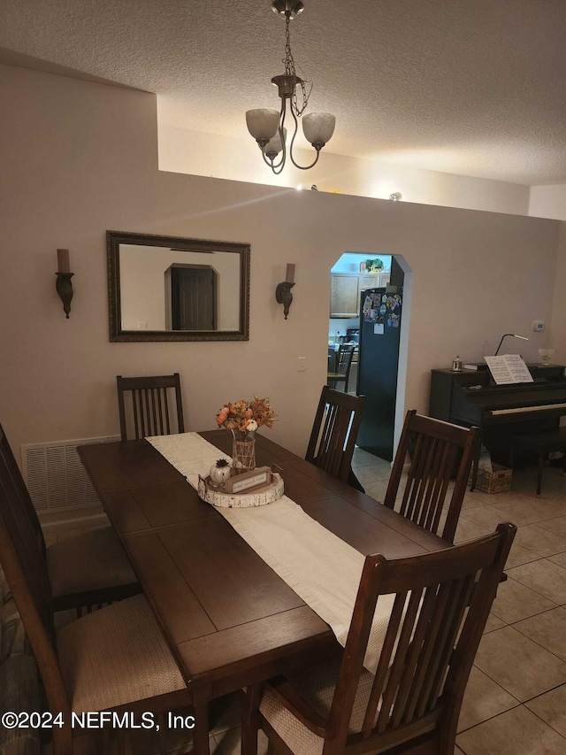 dining space with light tile patterned flooring, a textured ceiling, and an inviting chandelier