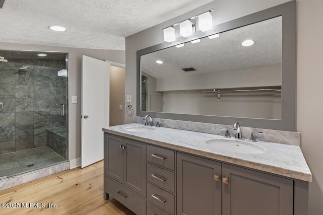 bathroom featuring vanity, wood-type flooring, a shower with door, and a textured ceiling