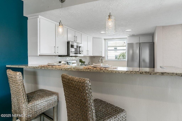 kitchen with pendant lighting, stainless steel appliances, white cabinets, a kitchen bar, and kitchen peninsula