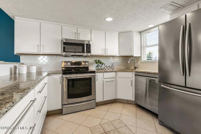 kitchen with light tile patterned floors, appliances with stainless steel finishes, white cabinetry, light stone counters, and decorative backsplash