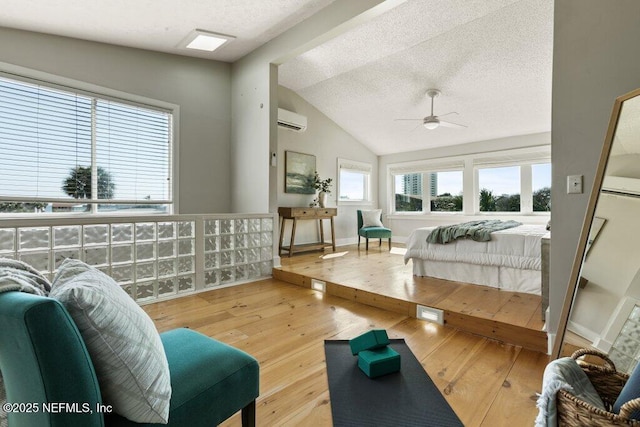 bedroom featuring vaulted ceiling, a textured ceiling, a wall unit AC, and light hardwood / wood-style floors