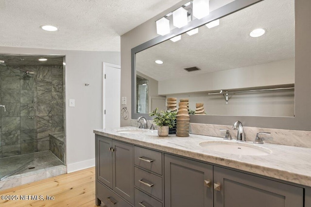 bathroom with hardwood / wood-style floors, vanity, a shower with door, and a textured ceiling