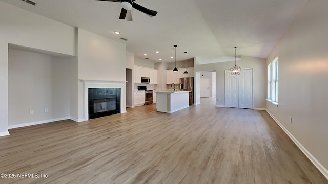 unfurnished living room featuring a fireplace, ceiling fan with notable chandelier, light hardwood / wood-style floors, and lofted ceiling