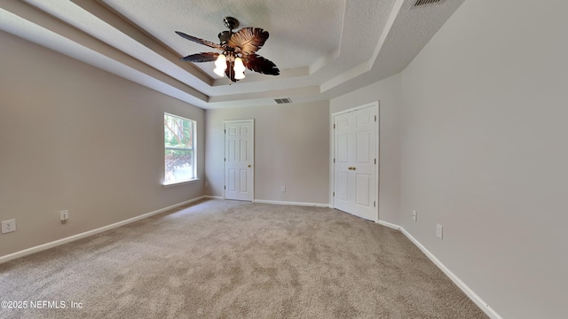 carpeted spare room featuring a raised ceiling, ceiling fan, and a textured ceiling