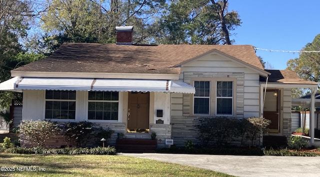 view of front of house featuring a shingled roof, entry steps, stone siding, and a chimney