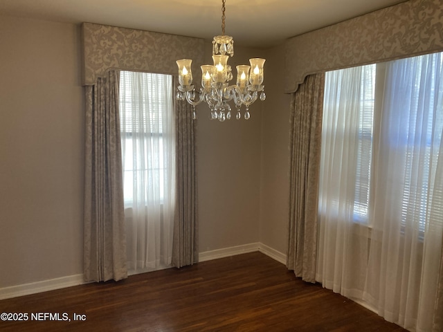 unfurnished room with plenty of natural light, dark wood-type flooring, and a chandelier