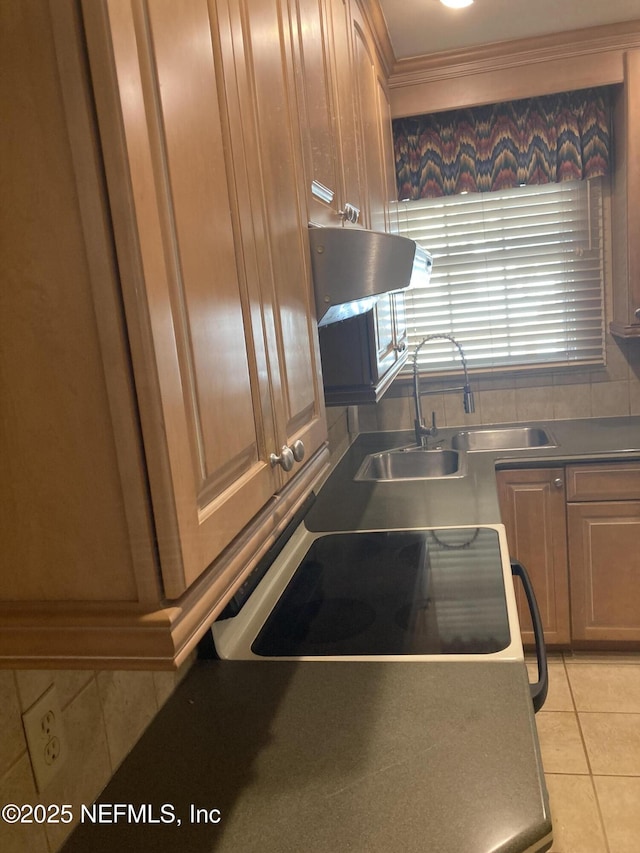 kitchen with light tile patterned floors, range, exhaust hood, and sink