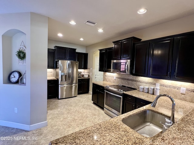 kitchen with stainless steel appliances, light stone counters, tasteful backsplash, and sink