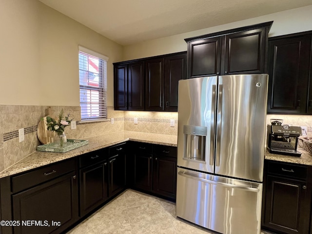 kitchen with stainless steel refrigerator with ice dispenser, light tile patterned floors, and light stone counters