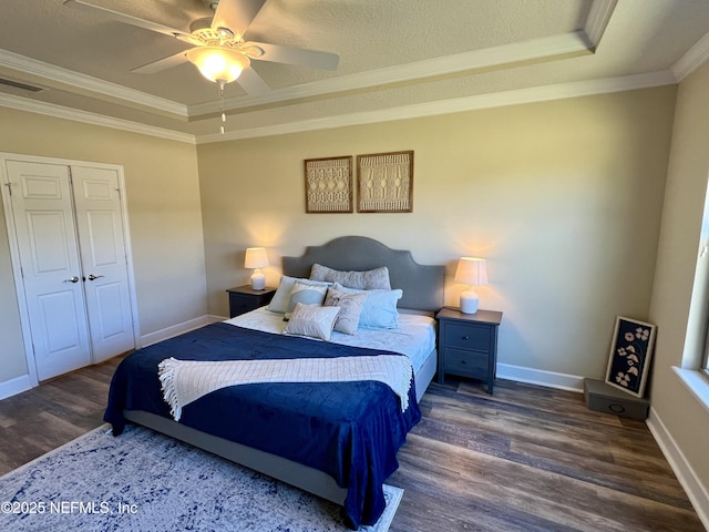 bedroom with ceiling fan, a raised ceiling, dark hardwood / wood-style flooring, crown molding, and a closet