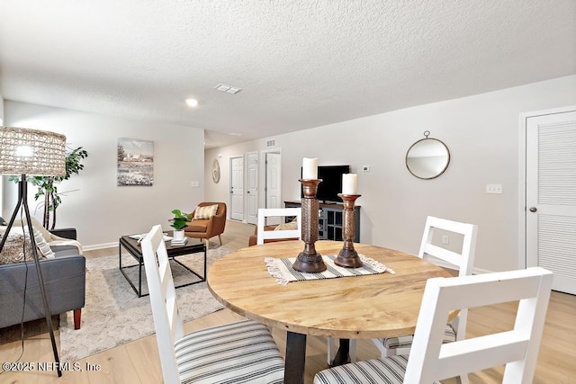 dining space with light hardwood / wood-style floors and a textured ceiling