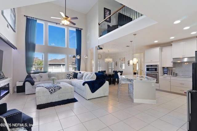 living room featuring light tile patterned floors, a high ceiling, and ceiling fan with notable chandelier