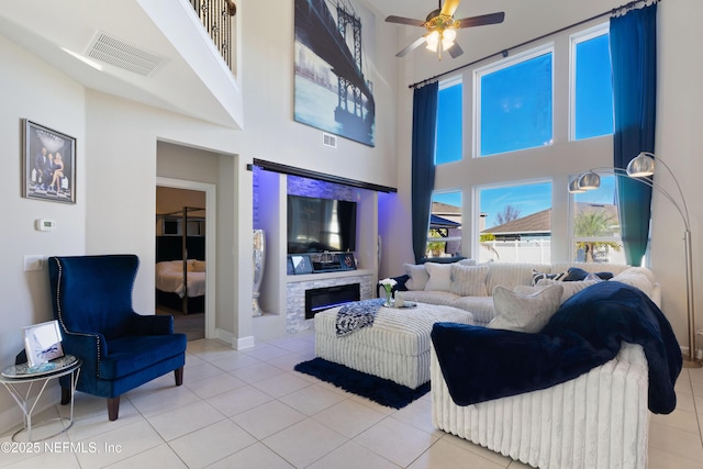 living room with ceiling fan, light tile patterned flooring, a fireplace, and a high ceiling