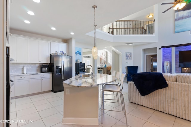 kitchen featuring white cabinets, stainless steel refrigerator with ice dispenser, decorative backsplash, and a center island with sink