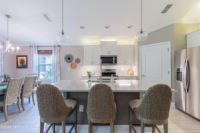 kitchen featuring white cabinetry, an island with sink, decorative light fixtures, and appliances with stainless steel finishes