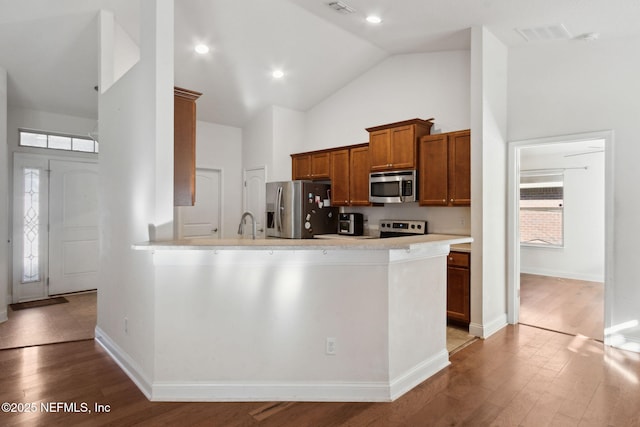 kitchen with sink, stainless steel appliances, high vaulted ceiling, kitchen peninsula, and light hardwood / wood-style floors