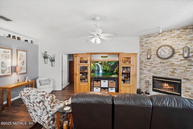 living room featuring ceiling fan, a large fireplace, dark wood-type flooring, and a textured ceiling