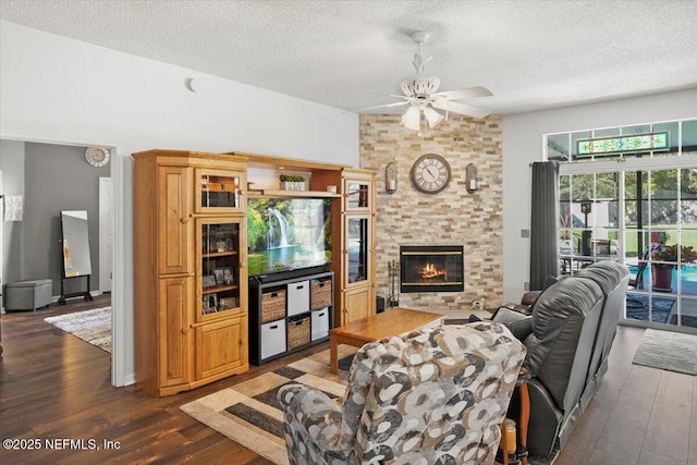 living room featuring ceiling fan, a large fireplace, dark hardwood / wood-style floors, and a textured ceiling