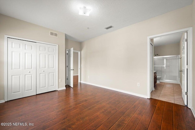 unfurnished bedroom featuring a textured ceiling, dark wood-type flooring, a closet, and ensuite bath