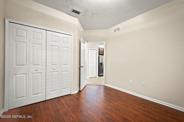 unfurnished bedroom featuring a closet, a textured ceiling, hardwood / wood-style flooring, and stainless steel fridge