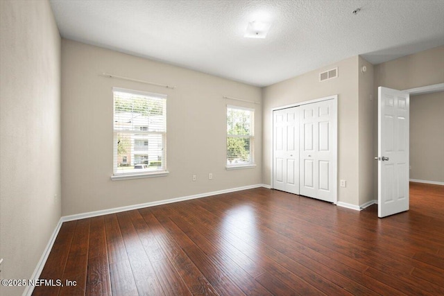 unfurnished bedroom featuring a closet, a textured ceiling, and dark wood-type flooring