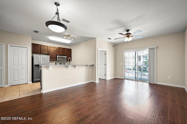 kitchen with a textured ceiling, ceiling fan, light hardwood / wood-style floors, hanging light fixtures, and appliances with stainless steel finishes