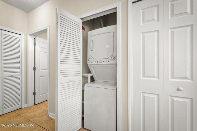 clothes washing area featuring stacked washer and dryer, a textured ceiling, and light tile patterned floors