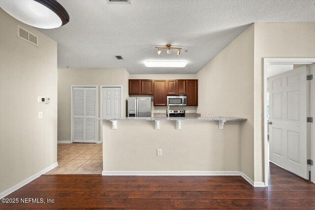 kitchen featuring stainless steel appliances, light stone countertops, dark hardwood / wood-style flooring, and a kitchen bar