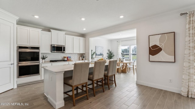 kitchen with a breakfast bar area, appliances with stainless steel finishes, white cabinetry, a center island with sink, and decorative backsplash