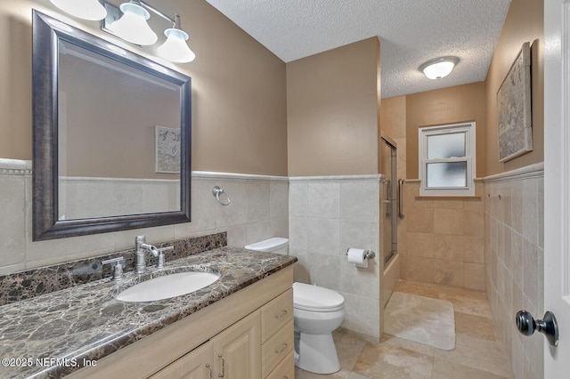 bathroom featuring a textured ceiling, vanity, tile walls, and toilet