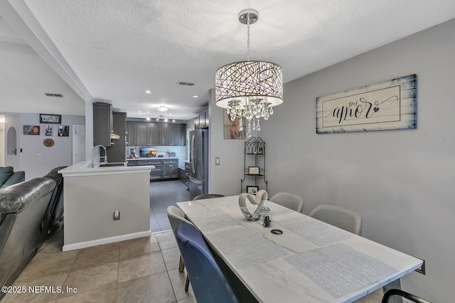 dining area featuring a textured ceiling, tile patterned floors, a notable chandelier, and sink