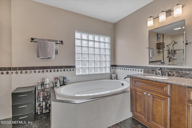 bathroom featuring a relaxing tiled tub, tile patterned floors, a textured ceiling, vanity, and tile walls