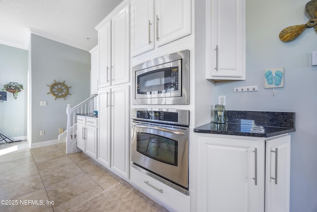 kitchen featuring stainless steel appliances, white cabinets, crown molding, dark stone counters, and light tile patterned flooring