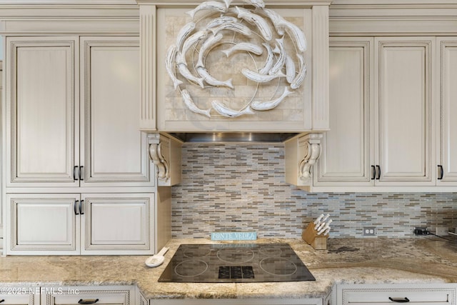 kitchen featuring black electric stovetop, light stone countertops, backsplash, and cream cabinetry