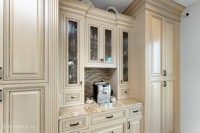 bar featuring backsplash, light stone counters, and cream cabinetry