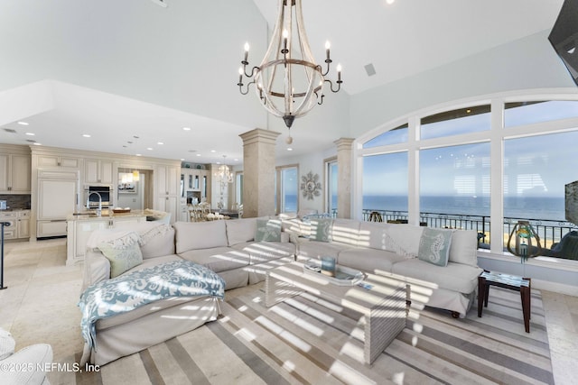 living room with a water view, ornate columns, a towering ceiling, and an inviting chandelier