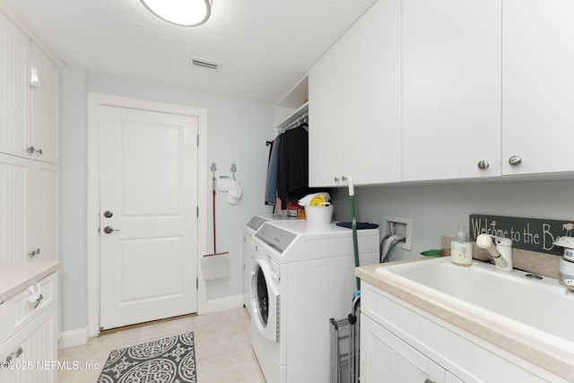 clothes washing area with sink, cabinets, separate washer and dryer, a textured ceiling, and light tile patterned floors