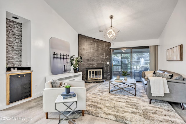 living room featuring sink, hardwood / wood-style floors, lofted ceiling, and a stone fireplace