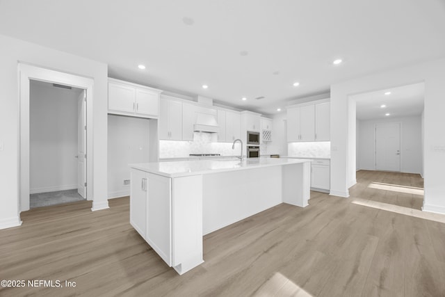 kitchen with decorative backsplash, appliances with stainless steel finishes, a center island with sink, white cabinets, and light hardwood / wood-style floors