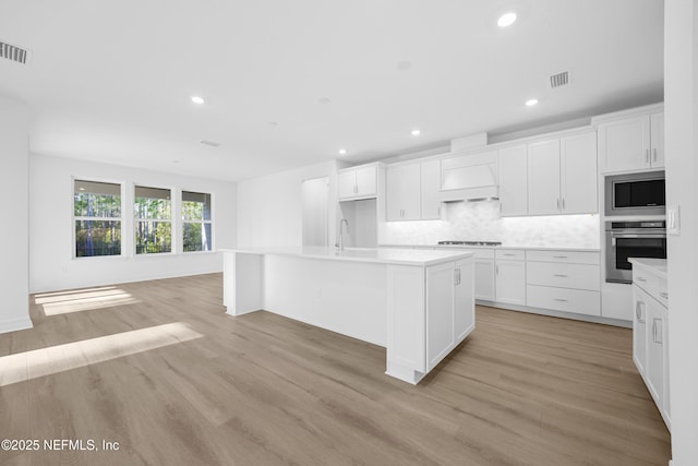 kitchen with light wood-type flooring, white cabinetry, an island with sink, and appliances with stainless steel finishes