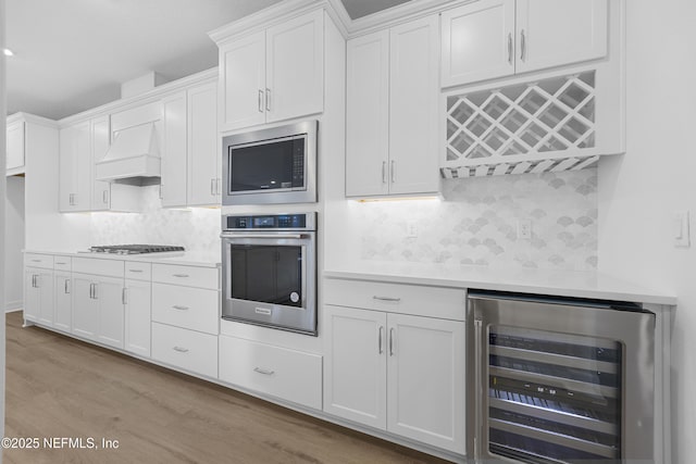 kitchen with custom exhaust hood, white cabinets, wine cooler, decorative backsplash, and stainless steel appliances