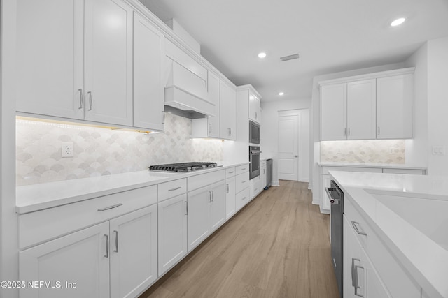 kitchen featuring white cabinets, custom range hood, light wood-type flooring, and stainless steel appliances