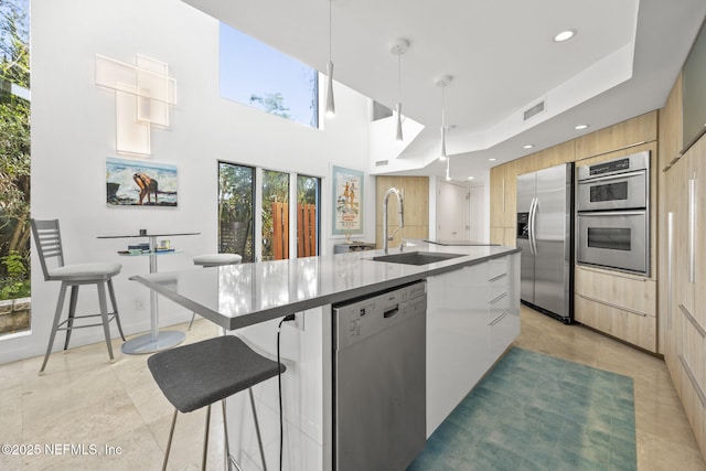 kitchen featuring sink, appliances with stainless steel finishes, a kitchen breakfast bar, pendant lighting, and a kitchen island with sink