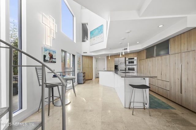 kitchen with appliances with stainless steel finishes, pendant lighting, a center island with sink, and a kitchen breakfast bar