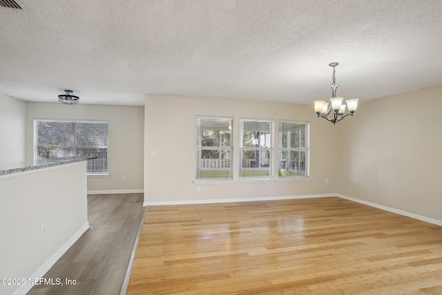 unfurnished dining area featuring a textured ceiling, hardwood / wood-style flooring, and a notable chandelier