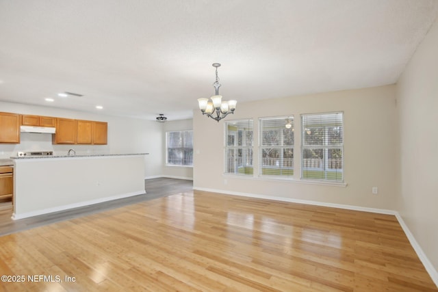 unfurnished living room with light hardwood / wood-style floors, a healthy amount of sunlight, and an inviting chandelier