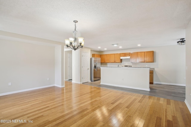 unfurnished living room featuring a notable chandelier, a textured ceiling, and light hardwood / wood-style flooring