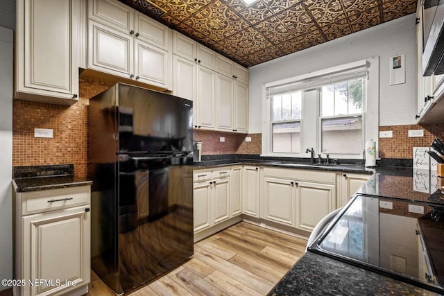 kitchen with black refrigerator, dark stone countertops, light wood-type flooring, and sink