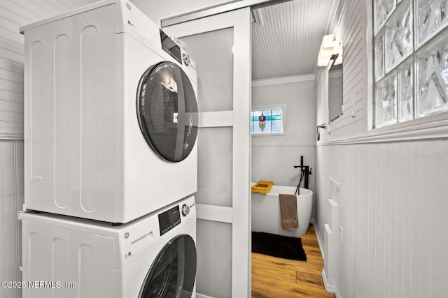 laundry room with crown molding, wood-type flooring, stacked washer and dryer, and wooden walls